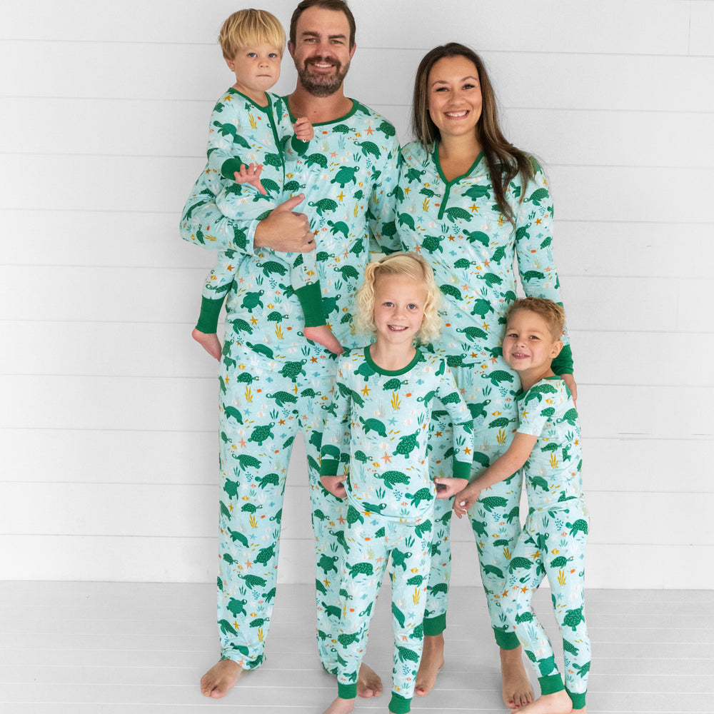 Image of a family of five wearing matching Sea Turtle Friends pjs. Mom and dad are wearing men's and women's tops and bottoms in Sea Turtle Friends print. Kids are wearing Sea Turtle Friends pjs in two piece and zippy styles