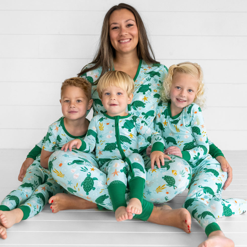 image of a Mom and her three kids. Mom is wearing women's tops and bottoms in Sea Turtle Friends print. Kids are wearing Sea Turtle Friends pjs in two piece and zippy styles