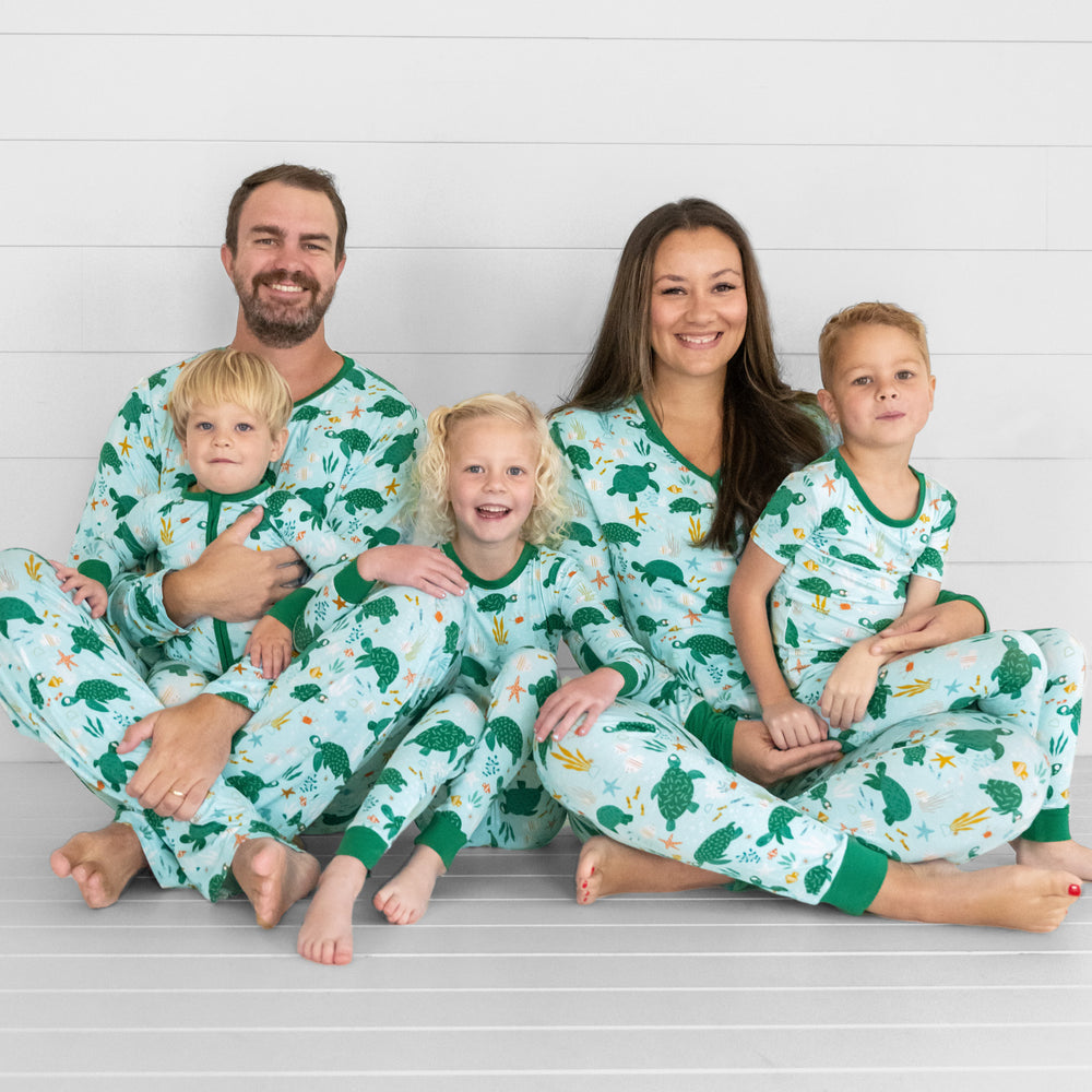 Image of a family of five sitting together wearing matching Sea Turtle Friends pjs. Mom and dad are wearing men's and women's tops and bottoms in Sea Turtle Friends print. Kids are wearing Sea Turtle Friends pjs in two piece and zippy styles