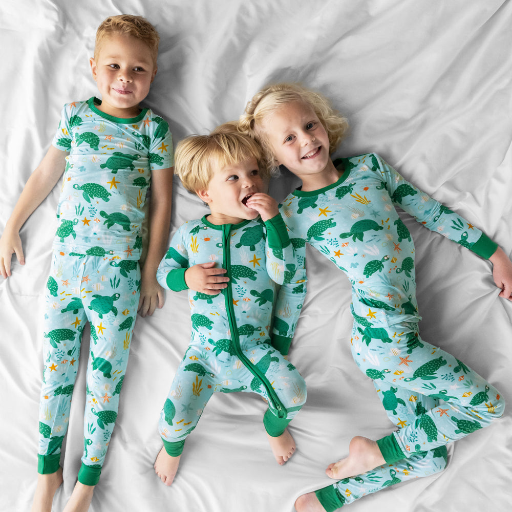 image of three children laying on a bed wearing Sea Turtle Friends pjs in two piece and zippy styles 