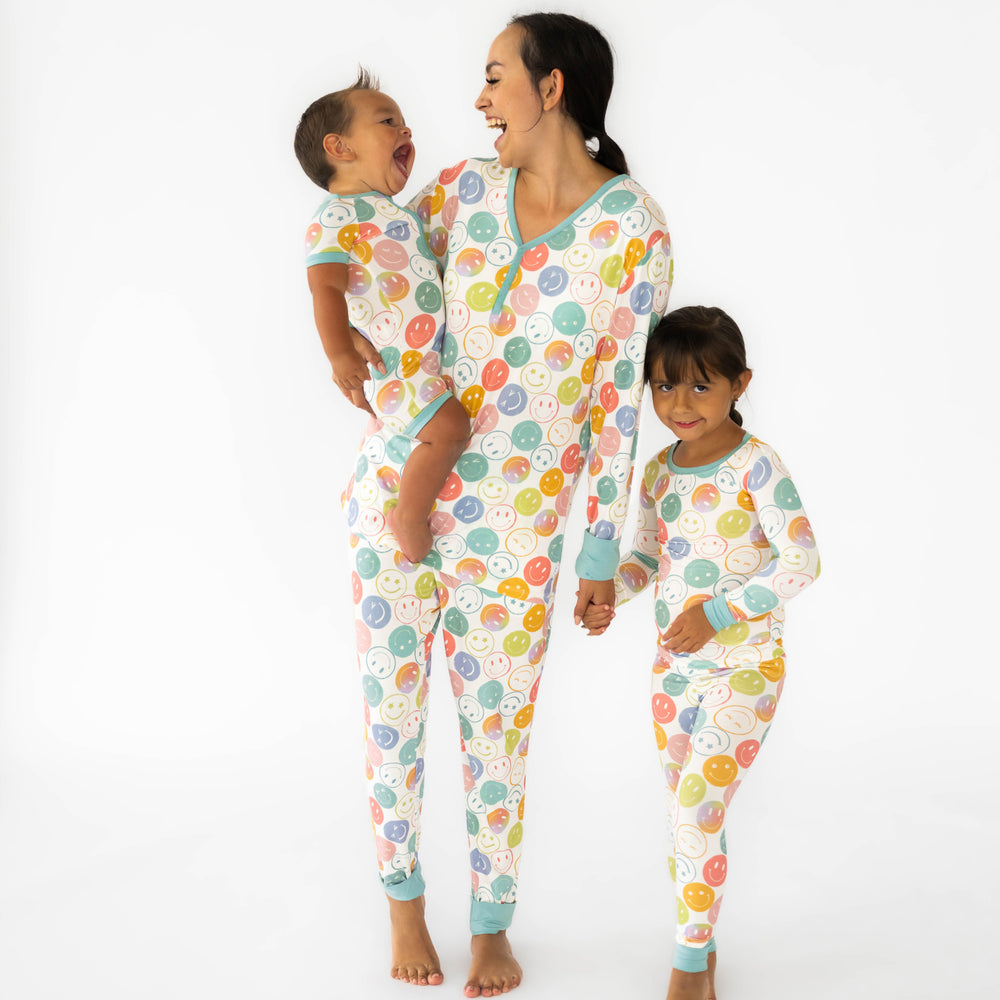 Mother and children wearing the Positive Vibes print. Baby is laughing and wearing the Positive Vibes Shorty Zippy while the mother is holding him in the Positive Vibes Women's Pajama Top & Pants. Girl on the right is wearing the Positive Vibes Two-piece Pajama Set