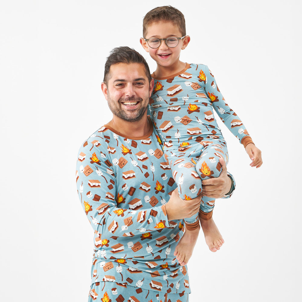 close up image of a man holding his child up wearing a S'mores Galore men's pj top, his child is wearing matching S'mores Galore two piece pj set