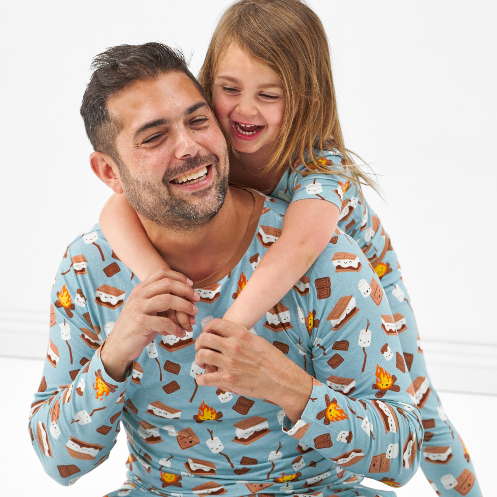 close up image of a man and his child up wearing a S'mores Galore men's pj top, his child is wearing matching S'mores Galore two piece pj set