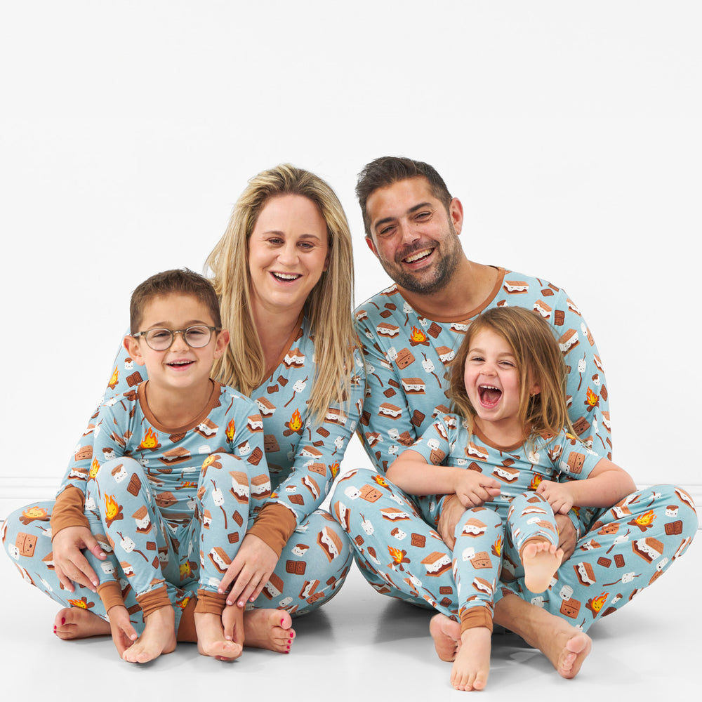 Close up image of a family of four sitting wearing matching S'mores Galore pjs in men's, women's, and children's two piece styles