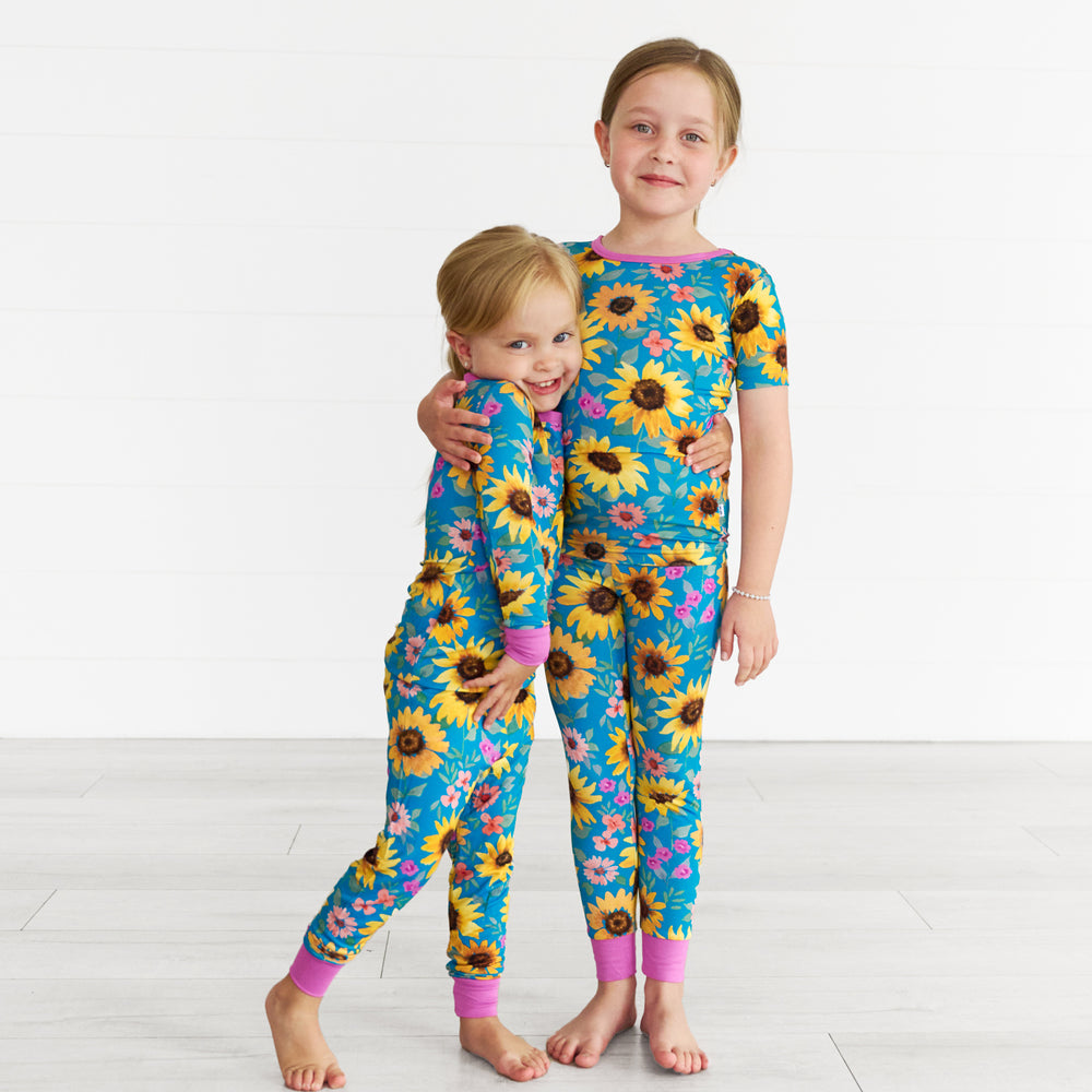 Girl on the left is wearing the Sunflower Fields Two-Piece Pajama Set and girl on the right is in the Sunflower Fields Two-Piece Short Sleeve Pajama Set