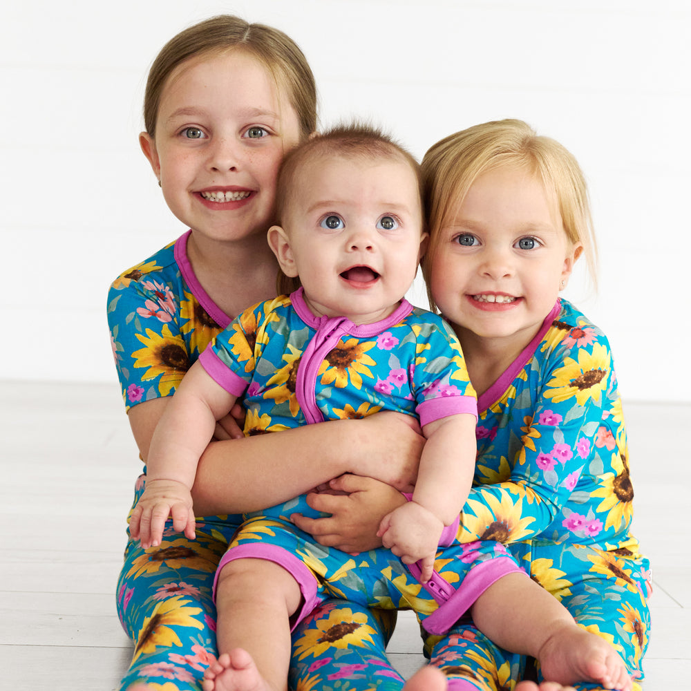 Girl on the left is wearing the Sunflower Fields Two-Piece Short Sleeve Pajamas. Baby in the middle is wearing the Sunflower Fields Shorty Zippy and girl on the left is in the Sunflower Fields Zippy