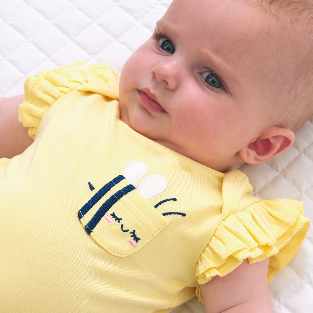 Close up image of a child laying on a bed wearing a Lemon Twist Graphic Flutter Bodysuit