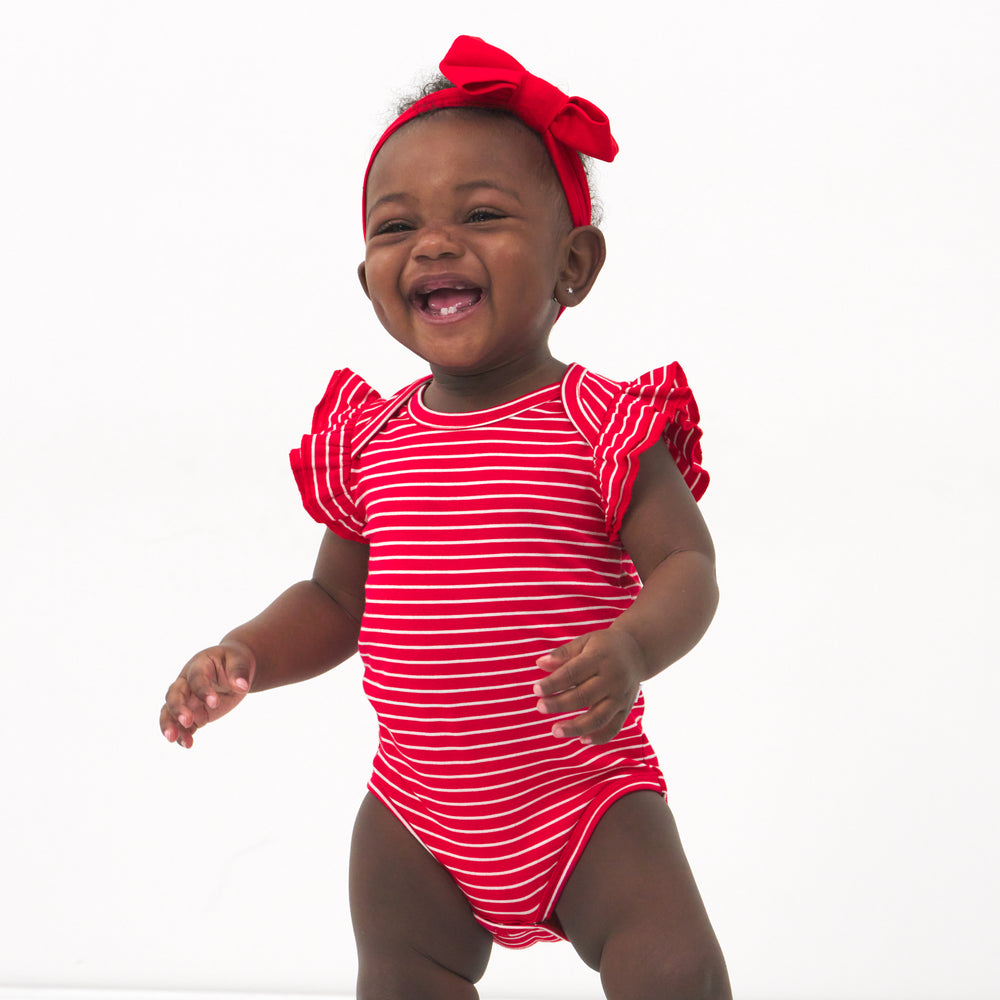 Child wearing a Candy Red Stripes flutter bodysuit and coordinating luxe bow headband