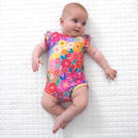 Child laying on a blanket wearing a Rainbow Blooms flutter bodysuit