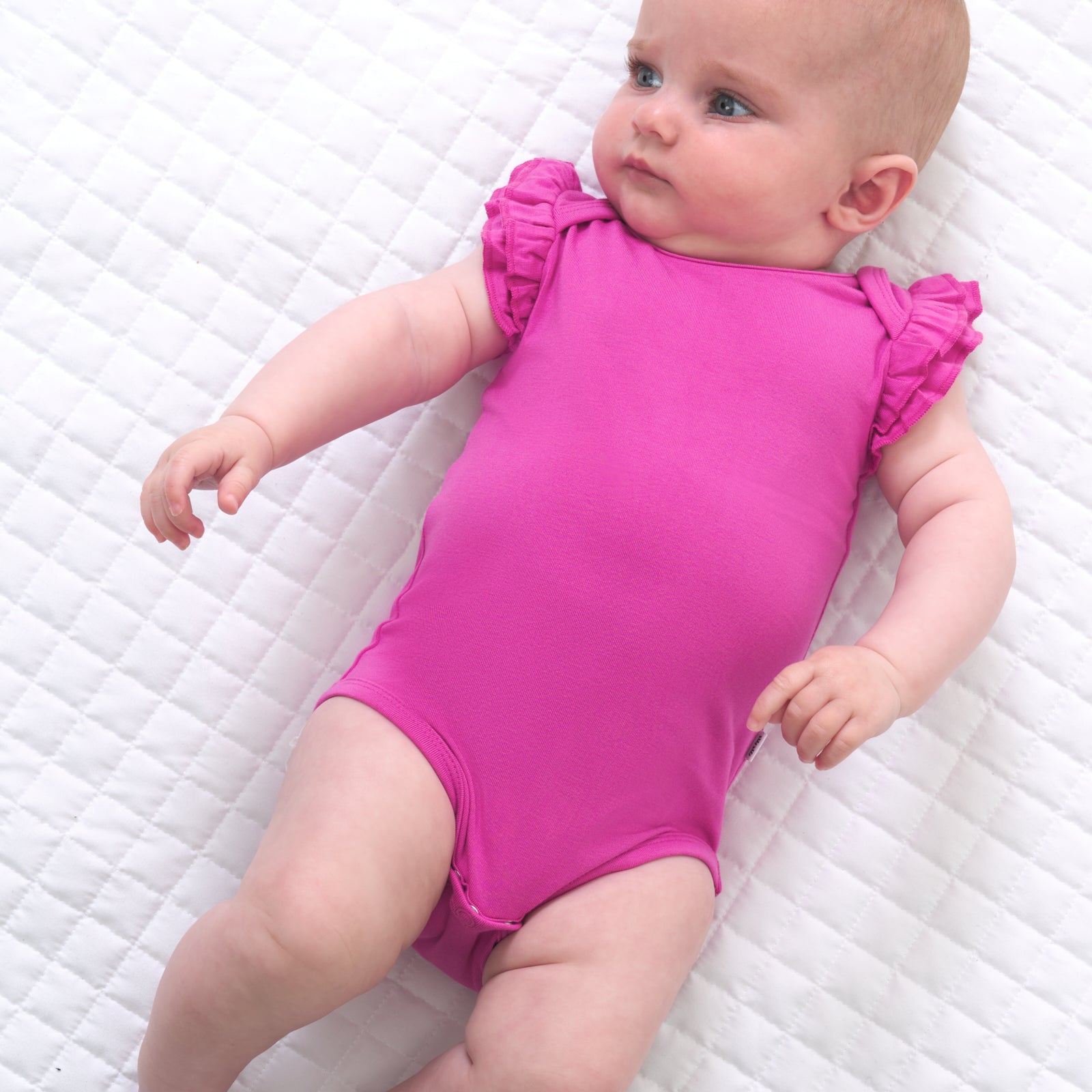 Child laying on a bed wearing a Rouge Pink flutter bodysuit