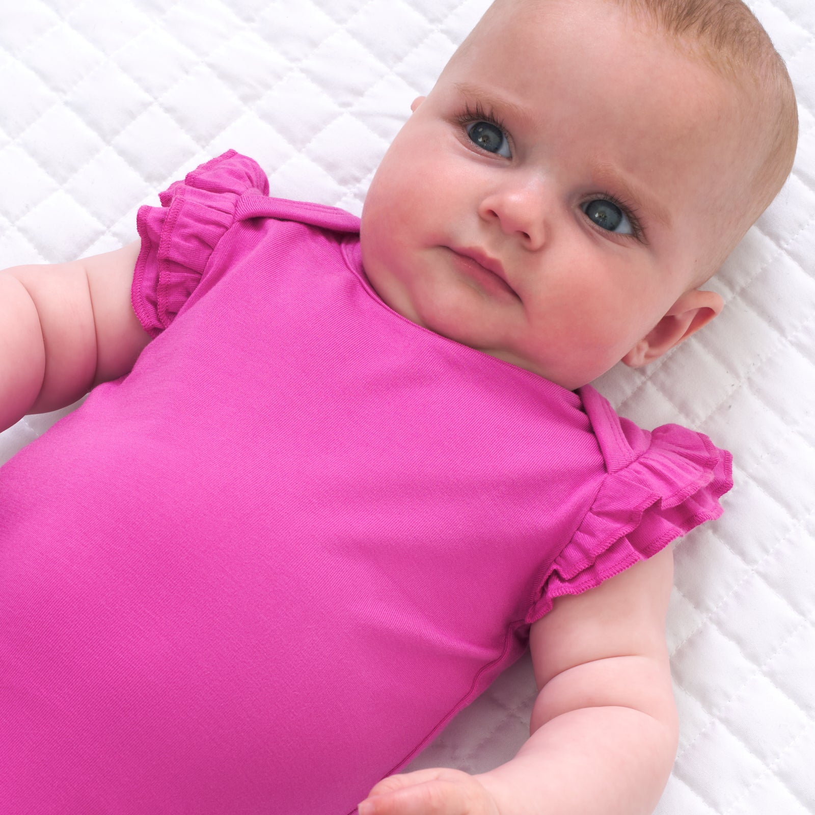 Close up image of a child laying on a bed wearing a Rouge Pink flutter bodysuit