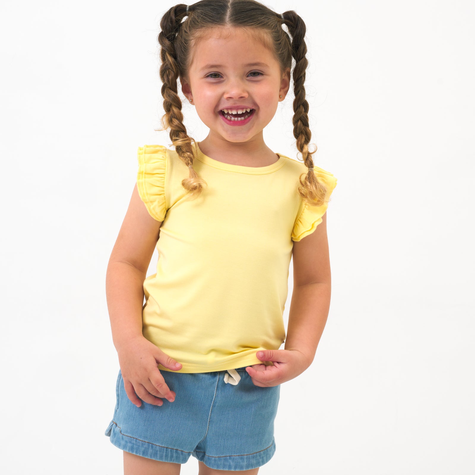 Close up image of a child wearing a Lemon Twist Flutter Tee paired with Light Denim shorts 