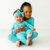 Two children cuddling wearing matching Glacier Turquoise pajamas in two piece and crescent zippy styles. One child is wearing a matching Glacier Turquoise luxe bow headband 