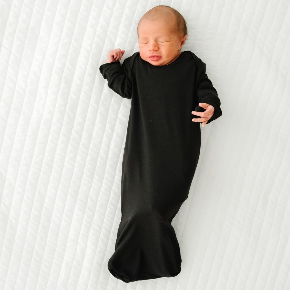 Child laying on a bed wearing a Black Infant Gown