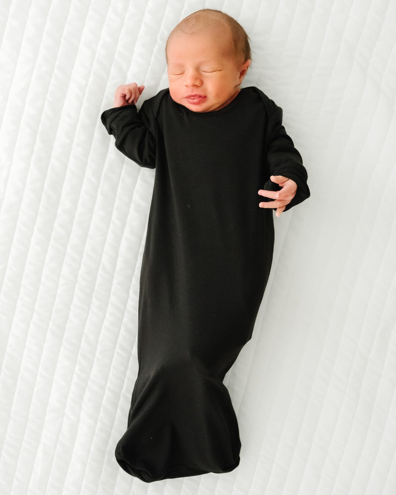 Child laying on a bed wearing a Black Infant Gown