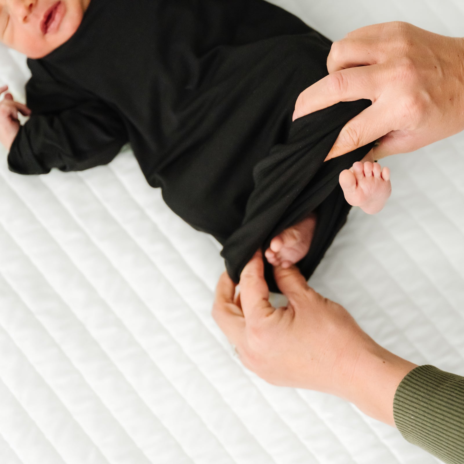 Child laying on a bed wearing a Black Infant Gown demonstrating the fold over bottom