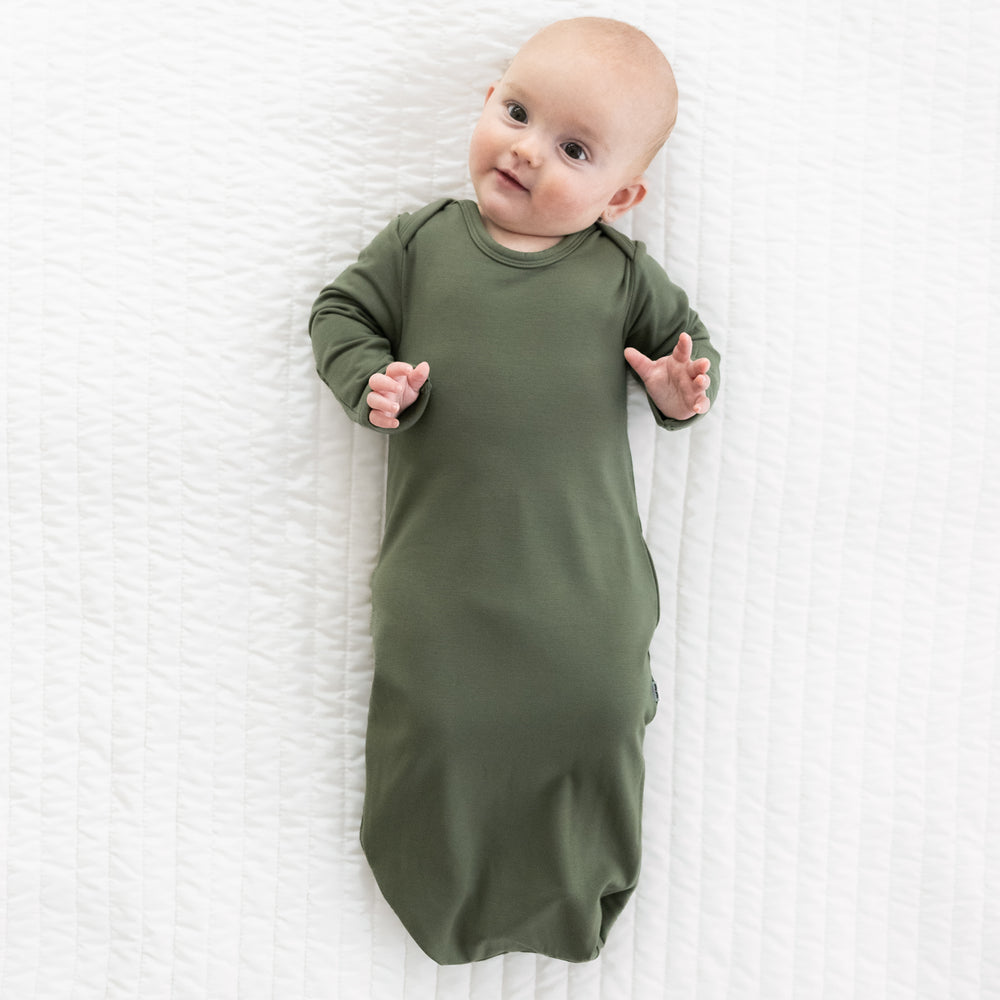 Child laying on a bed wearing a Cozy Olive infant gown