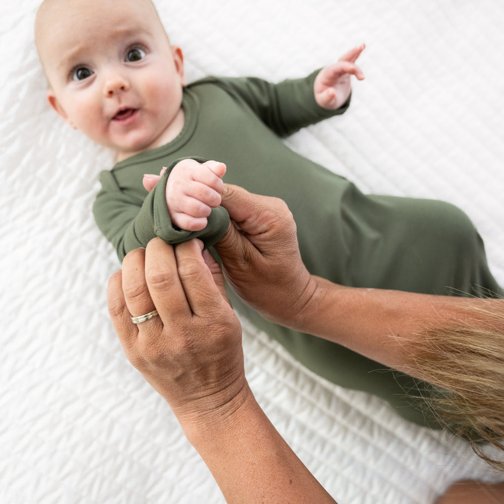 Child laying on a bed wearing a Cozy Olive infant gown. Mom is demonstrating the fold over mittens