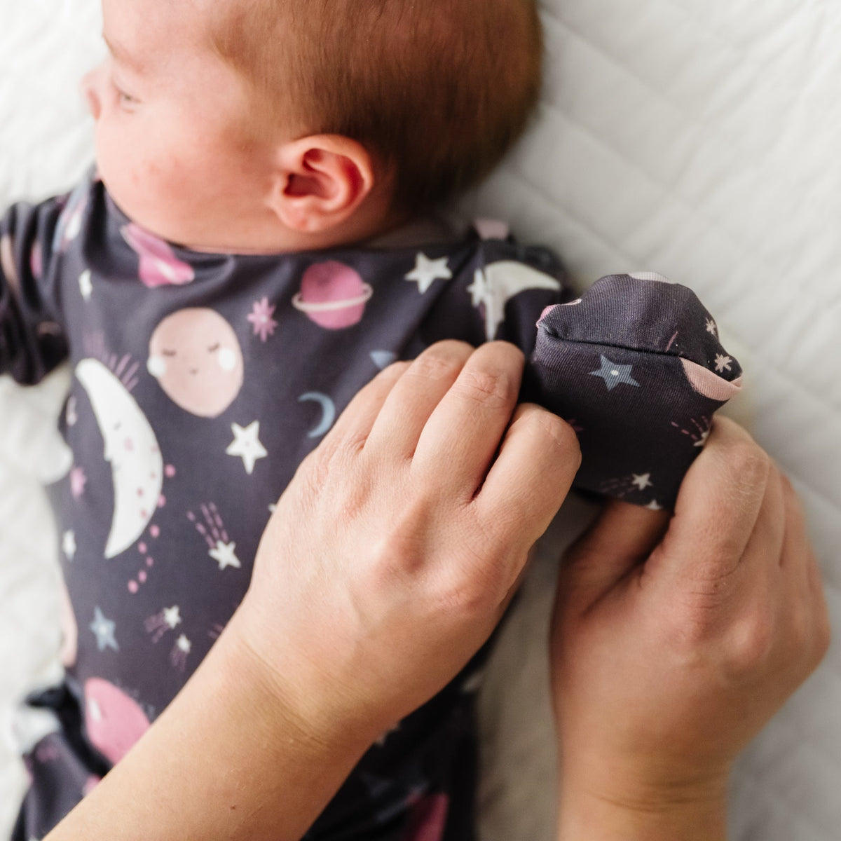 Child laying on a bed wearing a Pink To the Moon and Back Infant Gown demonstrating the fold over mittens
