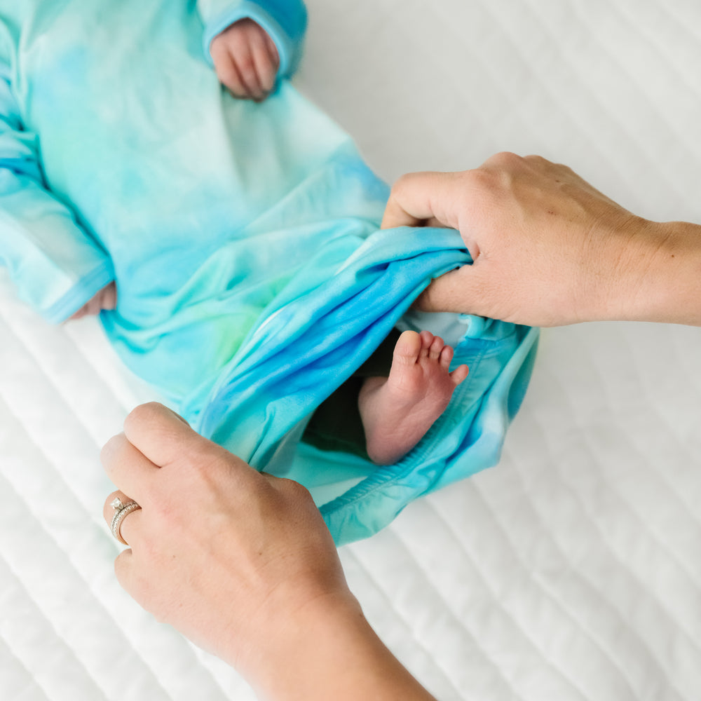 Close up image of a child laying on a bed wearing a Tidepool Infant Gown demonstrating the fold over bottom