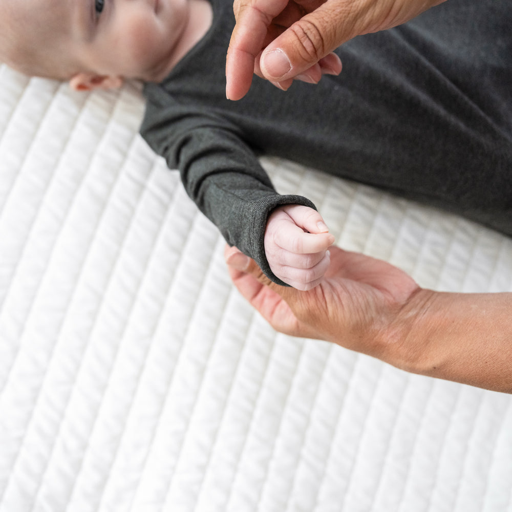 Secondary close up image of a child laying on a bed in a Cozy Heather Black infant gown. Child's mother is demonstrating the fold over mittens