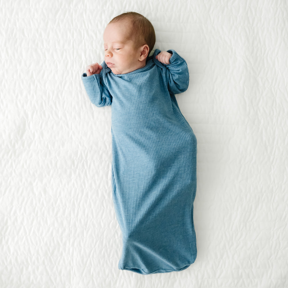 Child laying on a bed wearing a Heather Blue Ribbed Infant Gown