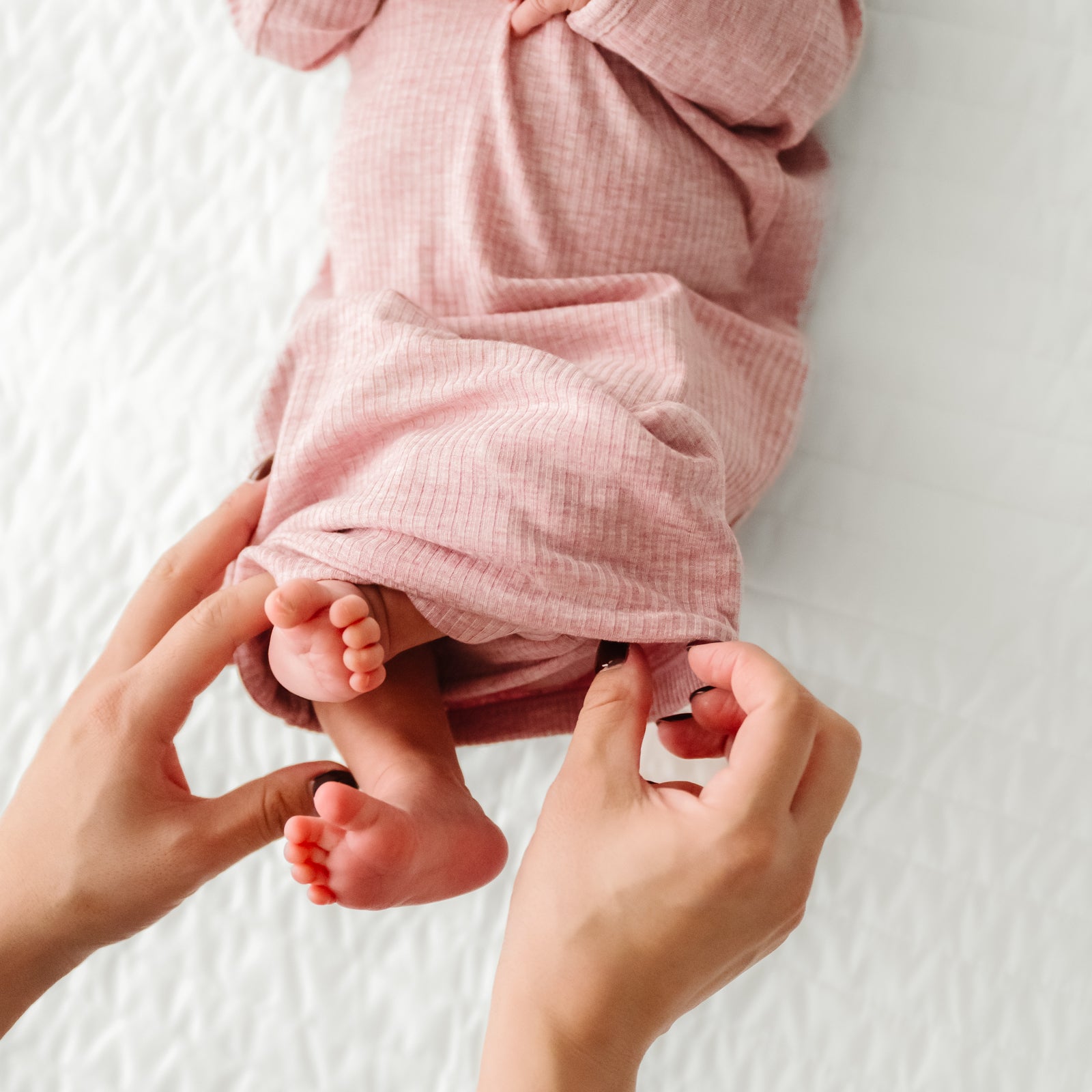 Child laying on a bed wearing a Heather Mauve Ribbed Infant Gown demonstrating the fold over bottom