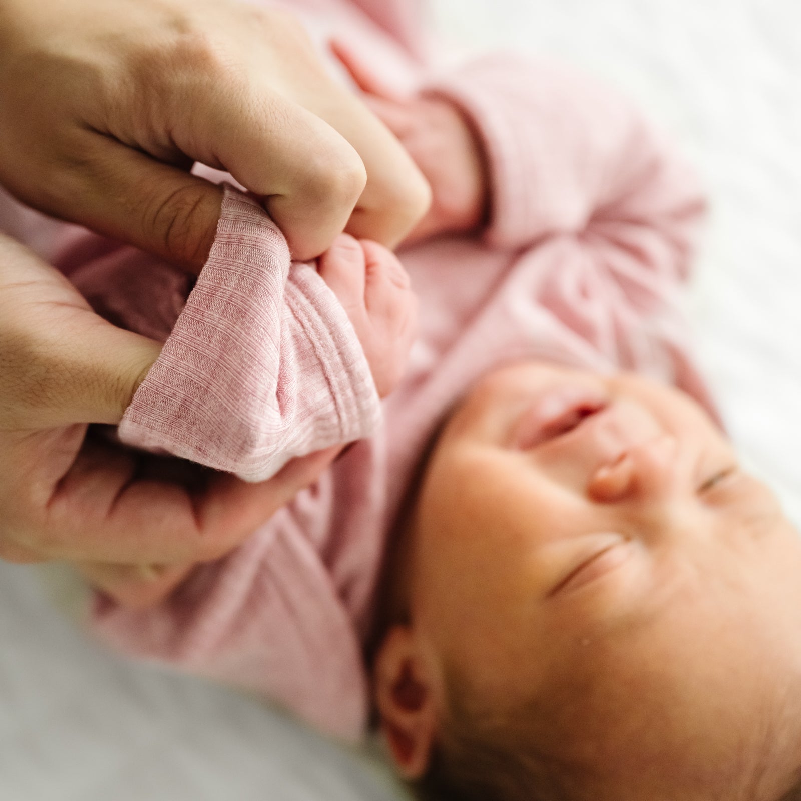 Child laying on a bed wearing a Heather Mauve Ribbed Infant Gown demonstrating the fold over mittens