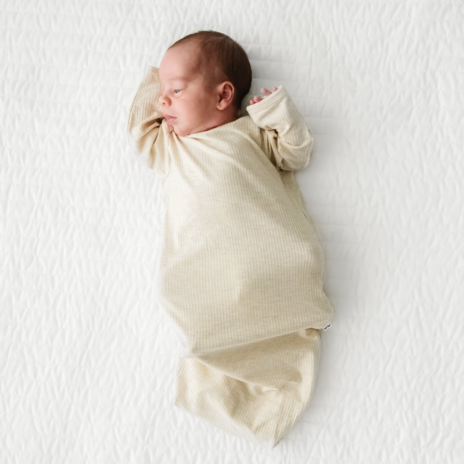 Child laying on a bed wearing a Heather Oatmeal Ribbed Infant Gown