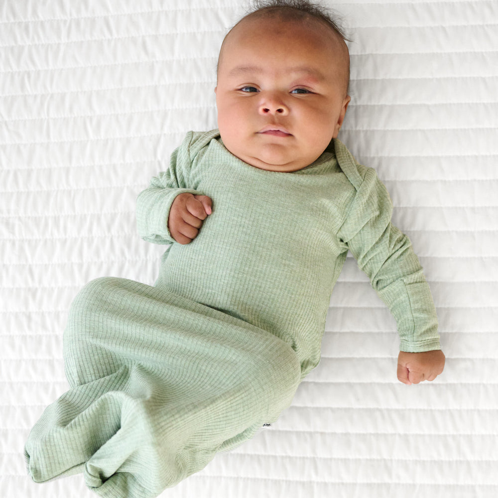 Child laying on a bed wearing a Heather Sage infant gown