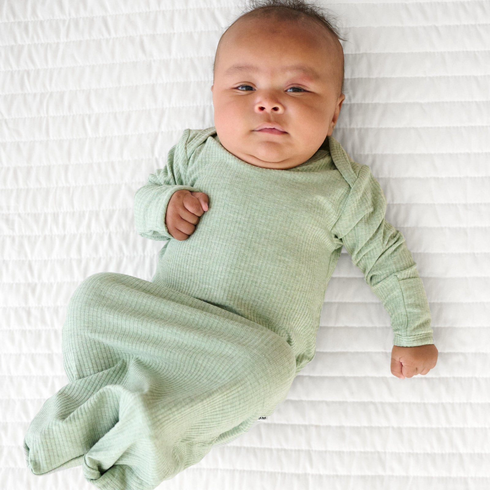 Child laying on a bed wearing a Heather Sage infant gown