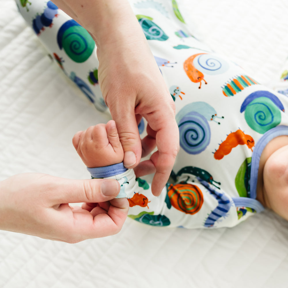 Close up image of an infant wearing an Inchin' Along infant gown with a parent folding over the mitten