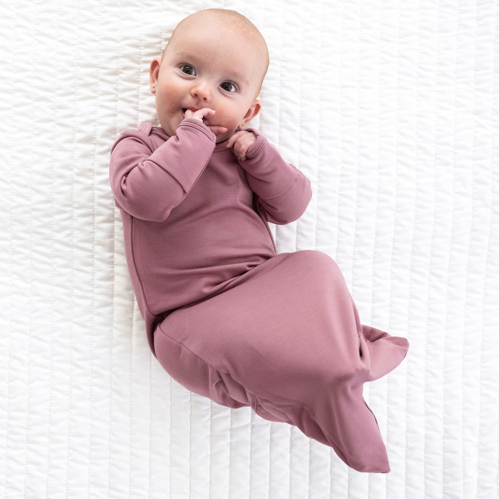 Child laying on a bed wearing a Cozy Dusty Plum infant gown