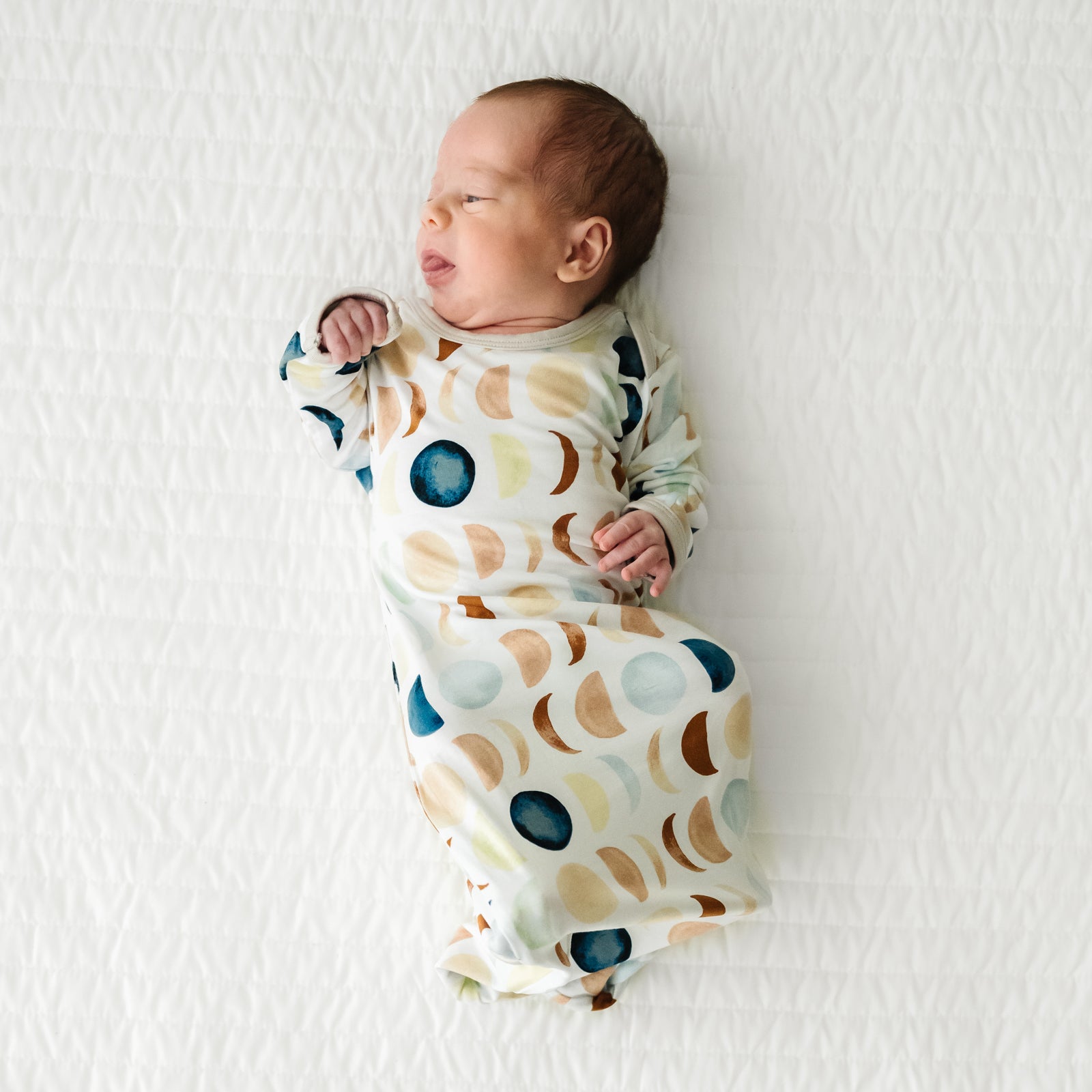 Child laying on a bed wearing a Luna Neutral infant gown
