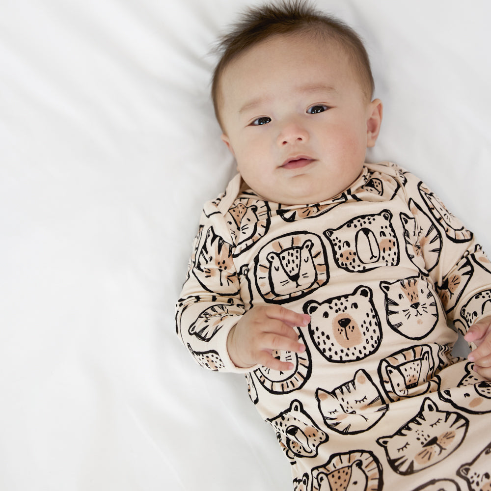 Close up image of a child laying on a bed wearing a Lions, Tigers, and Bears infant gown