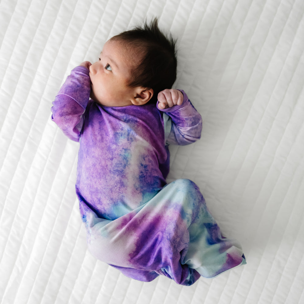 Child laying on a bed wearing a Purple Watercolor Infant Gown
