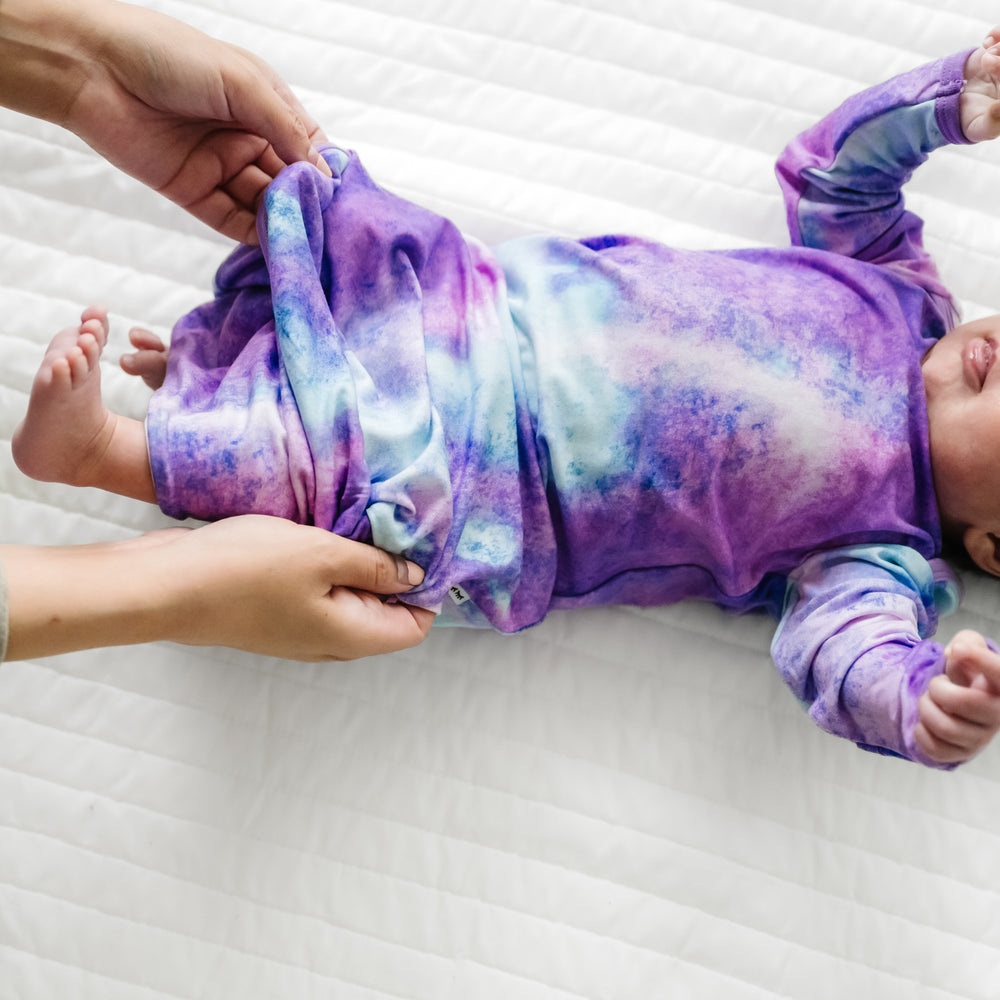Child laying on a bed wearing a Purple Watercolor Infant Gown demonstrating the fold over bottom