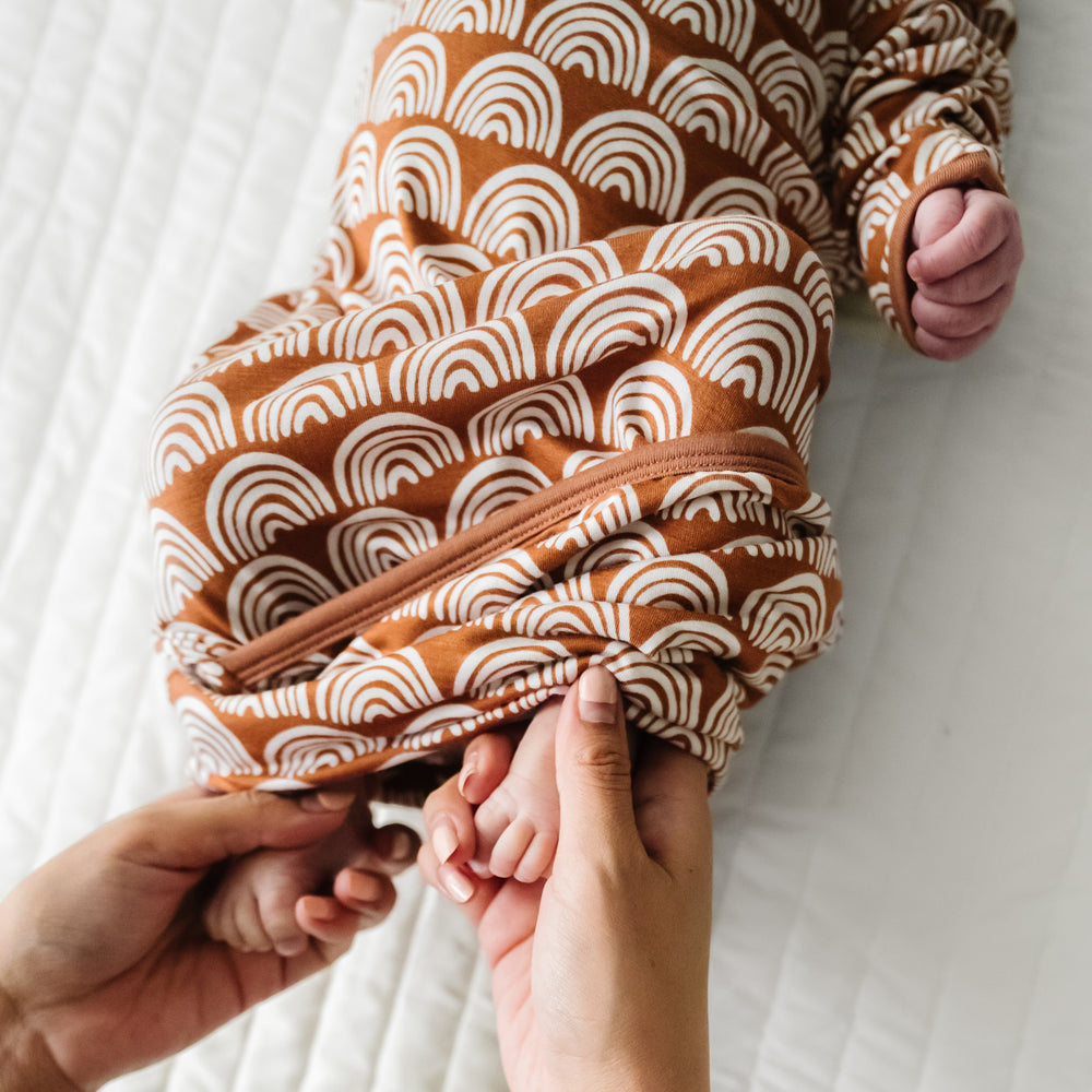 Child laying on a bed wearing a Rust Rainbows Infant Gown demonstrating the fold over bottom