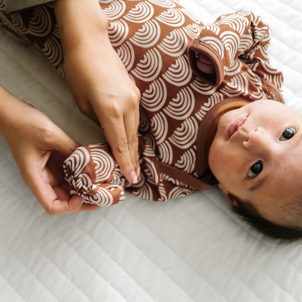 Child laying on a bed wearing a Rust Rainbows Infant Gown demonstrating the fold over mittens