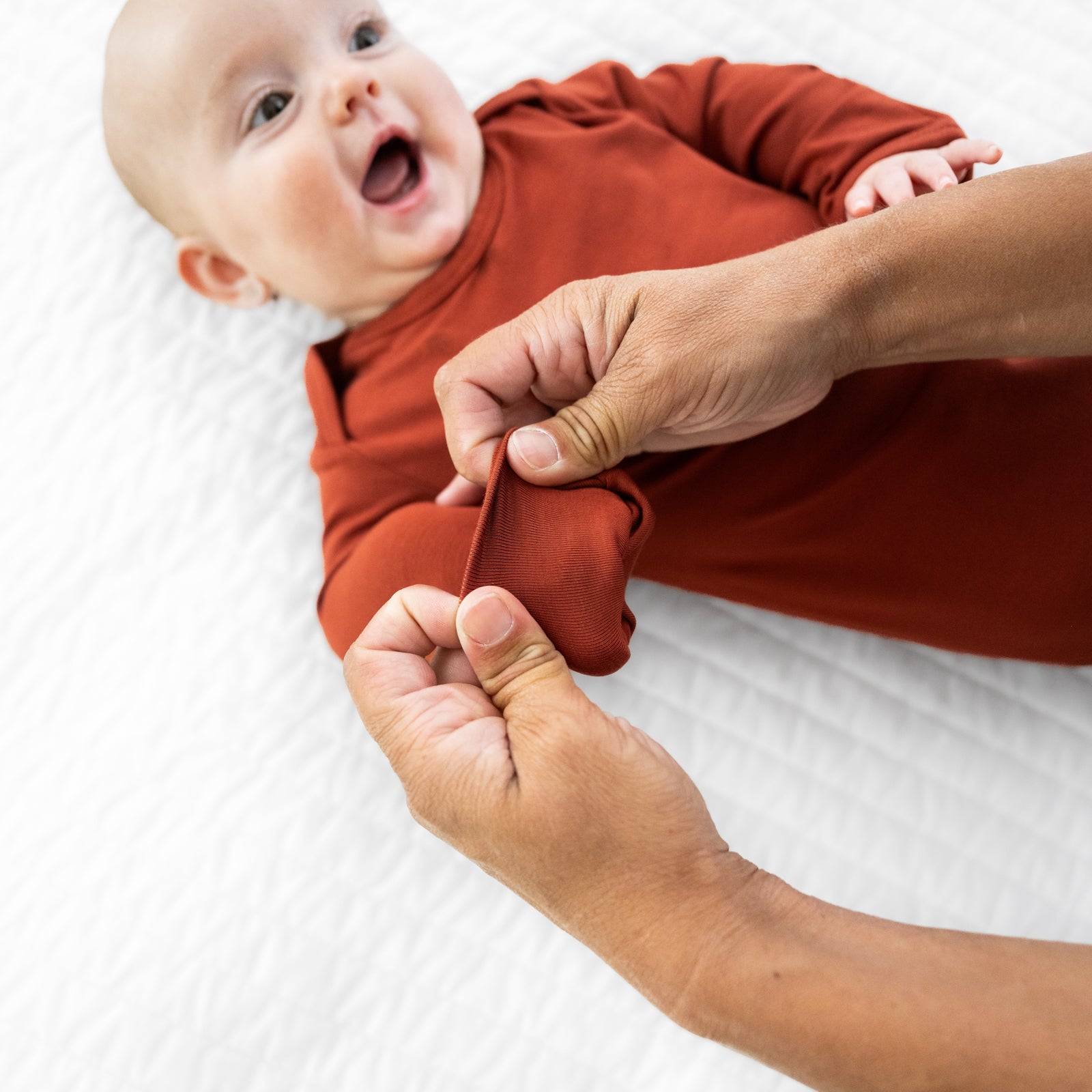 Child wearing a Cozy Rust infant gown. Mom is showing the folded mitten cuff