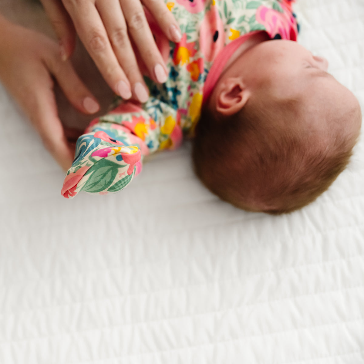 Child laying on a bed wearing a Secret Garden Infant Gown demonstrating the fold over mittens