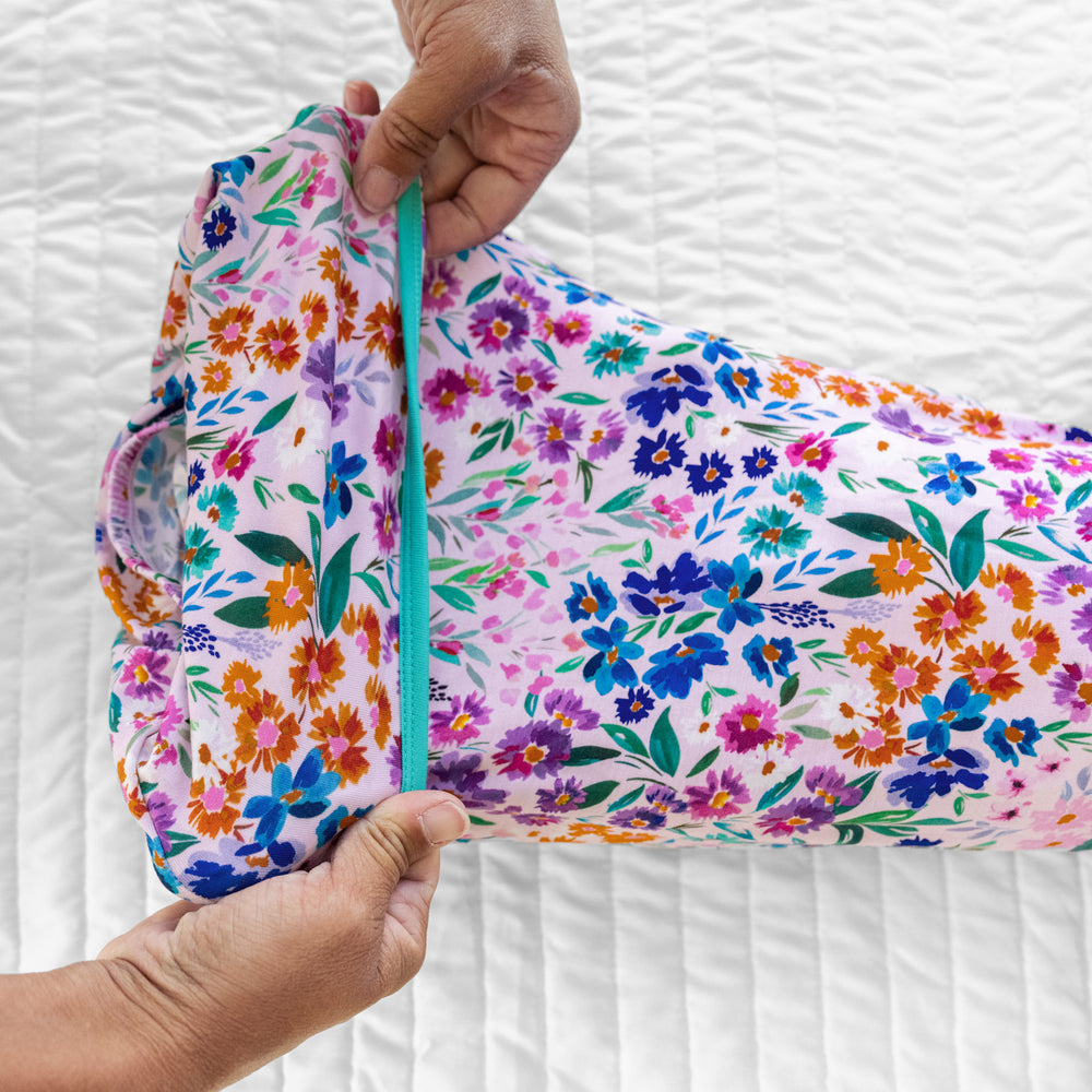 Close up image of a child laying on a bed wearing a Sweet Pea Floral infant gown. Mom is showing the fold over foot envelope