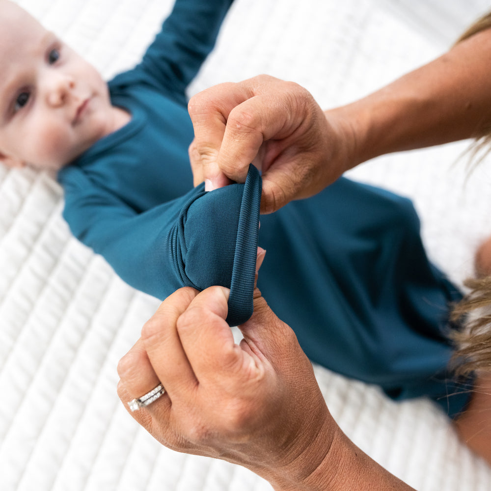 Alternate image of a child laying on a bed wearing a Cozy Twilight Teal infant gown. Mom is demonstrating the fold over mittens