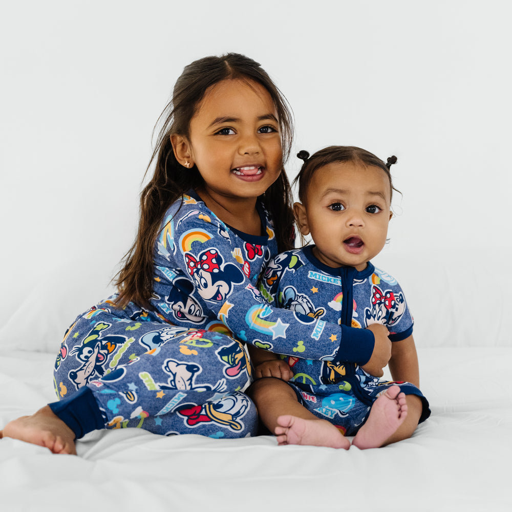 Two children sitting on a bed wearing matching Navy Disney Mickey's Clubhouse bamboo pajamas