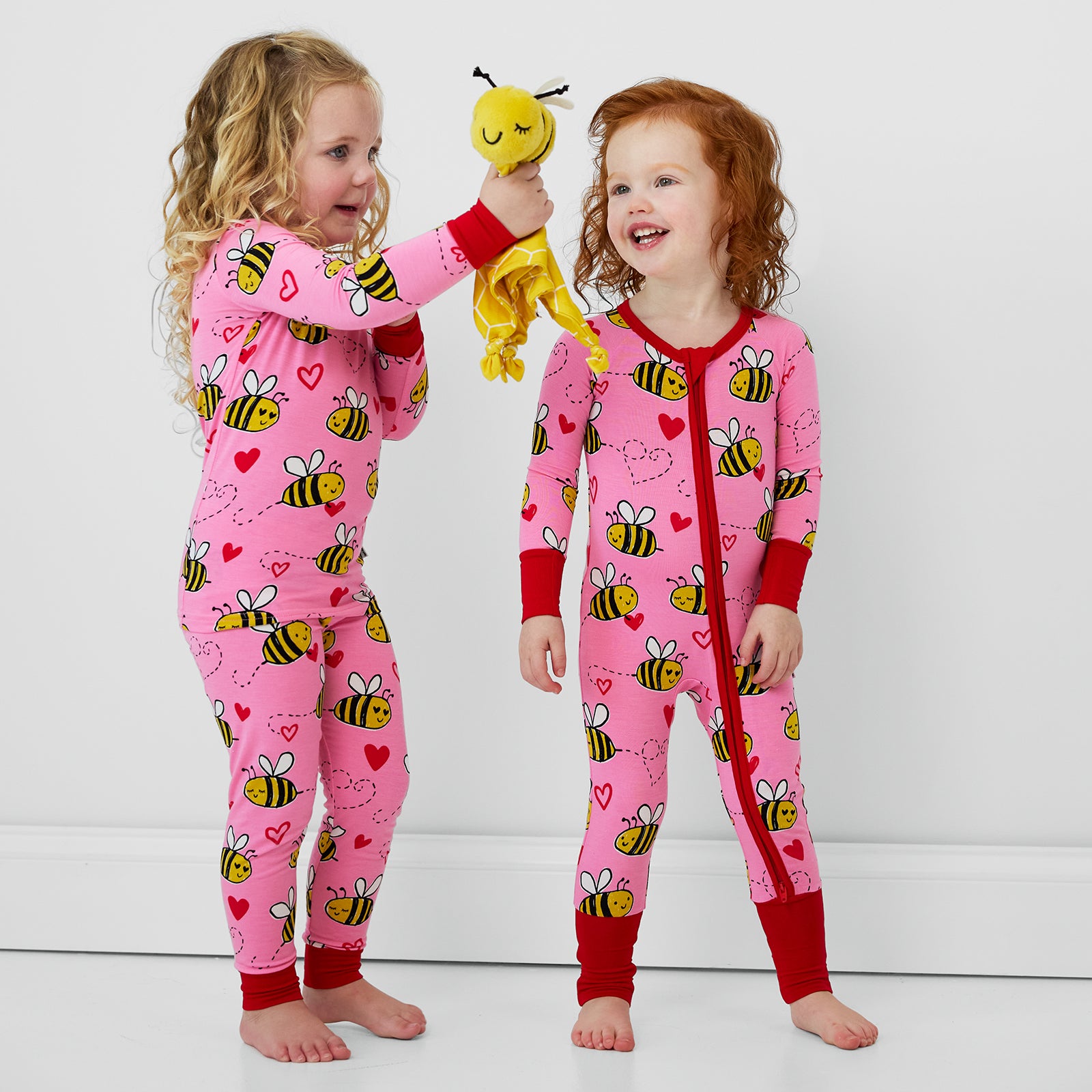 two children wearing Bee Mine pjs in zippy and two piece styles holding a Honey the Bumble Bee Lovey