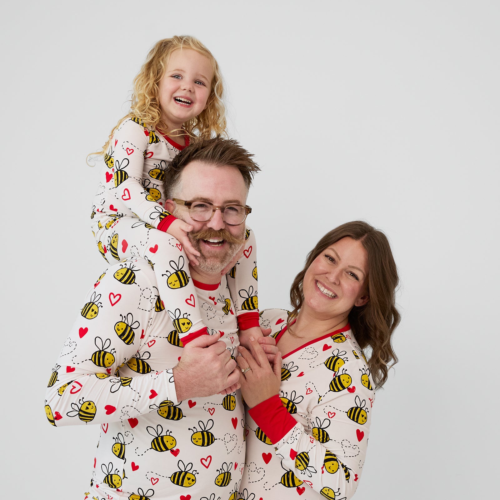 close up image of a family of three wearing matching Bee Mine pjs in women's, men's, and children's two piece styles