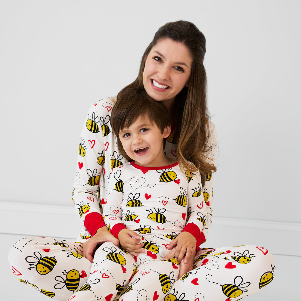 Close up image of a mom sitting with her child. They're wearing matching Bee Mine printed pjs in women's and children's two piece styles