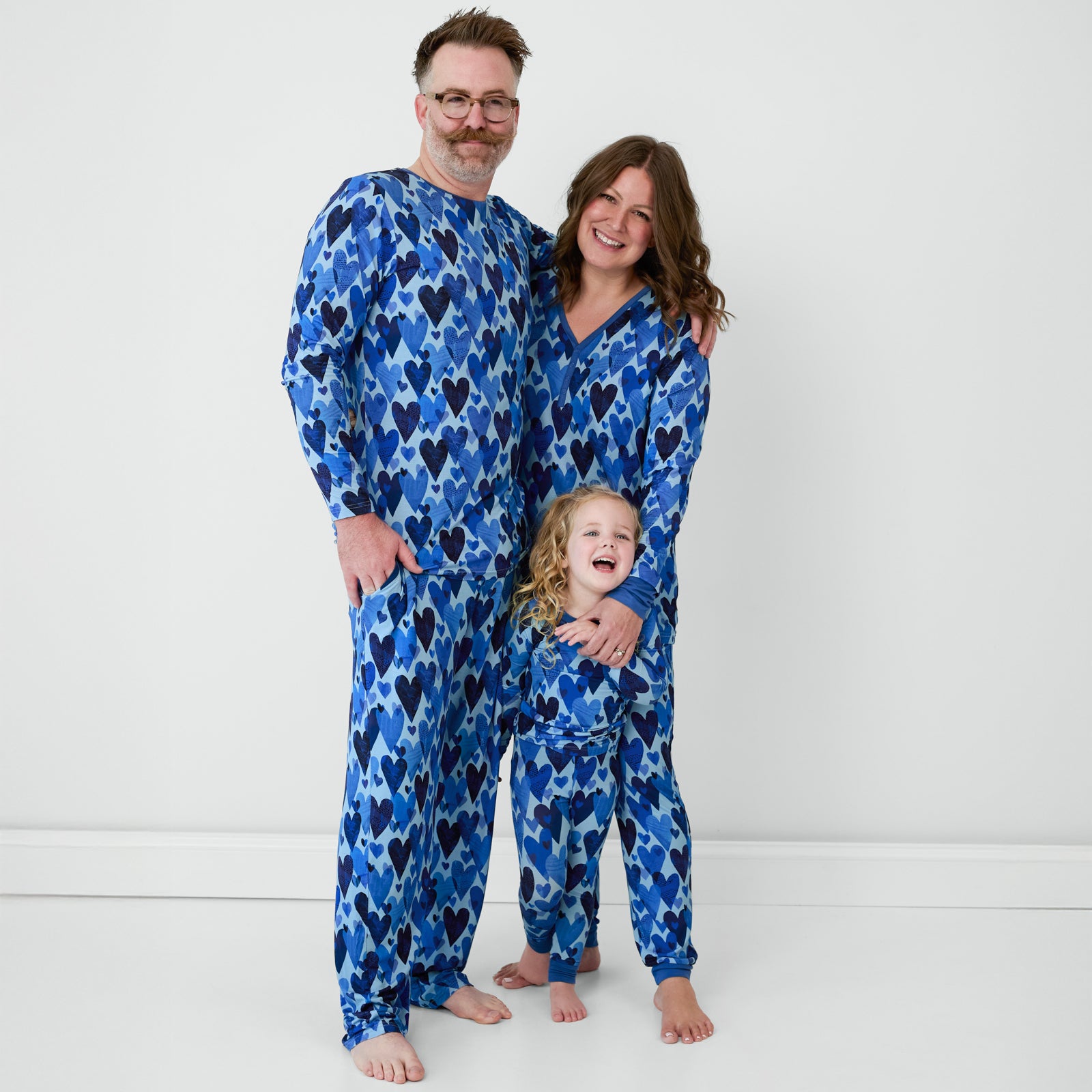 Family standing matching in men's, women's and children's Blue Hearts & Crafts pajamas.