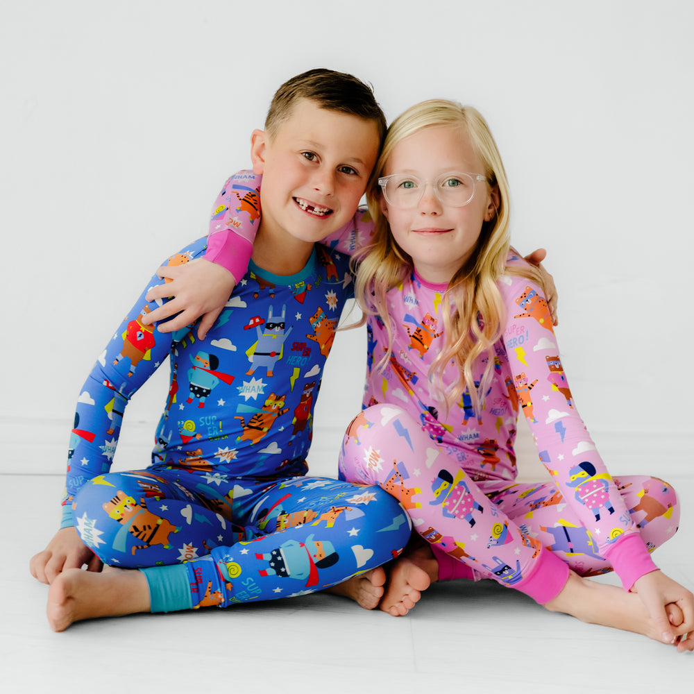 Two children sitting wearing matching pink and blue Sleepy Heroes Two-Piece PJ Sets