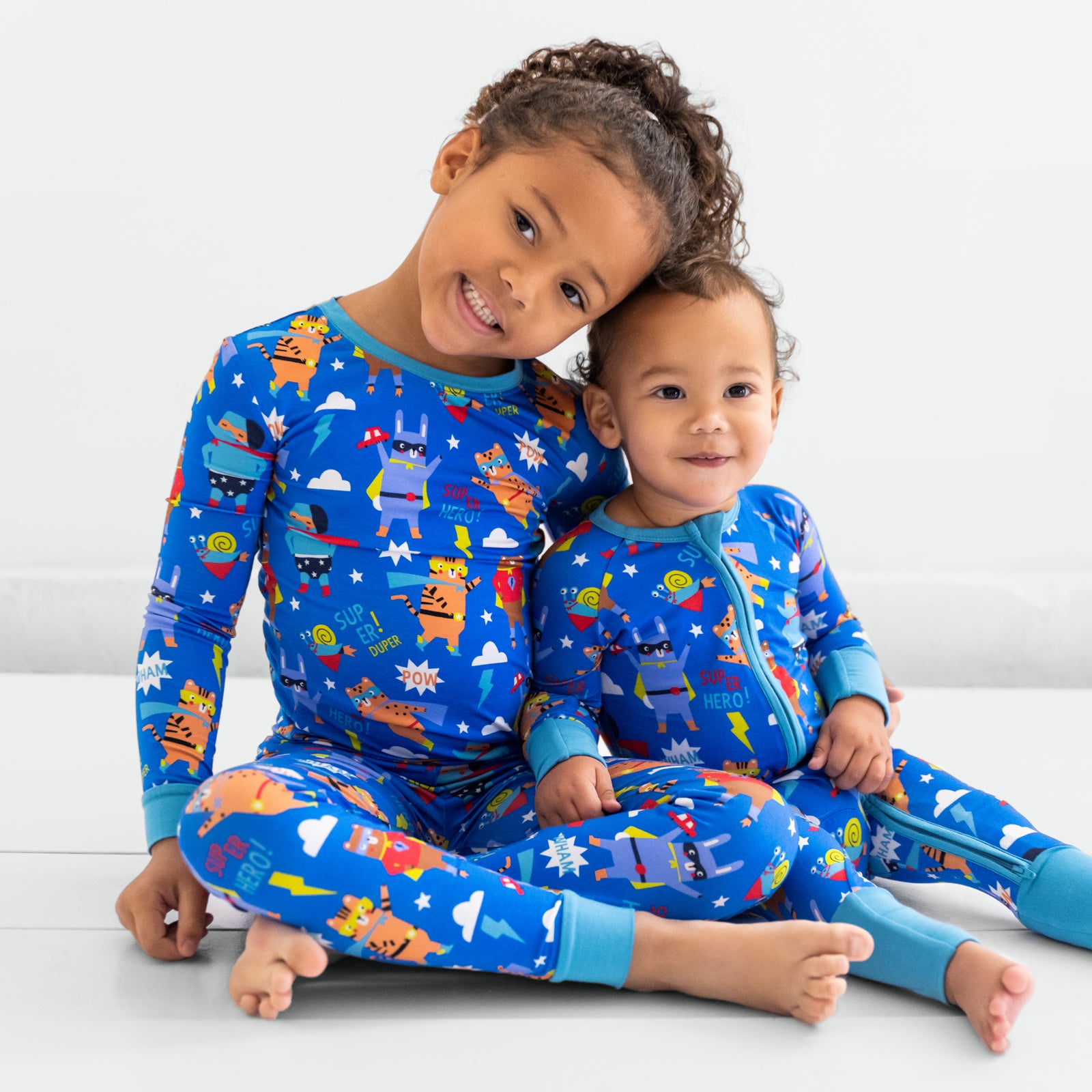 Two children sitting wearing matching Blue Sleepy Heroes styles